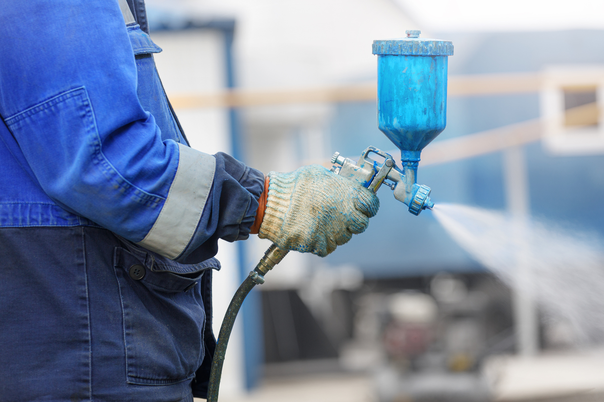 Spray gun in hand. A worker in overalls and a glove holds a spray compressor for painting in his hand.